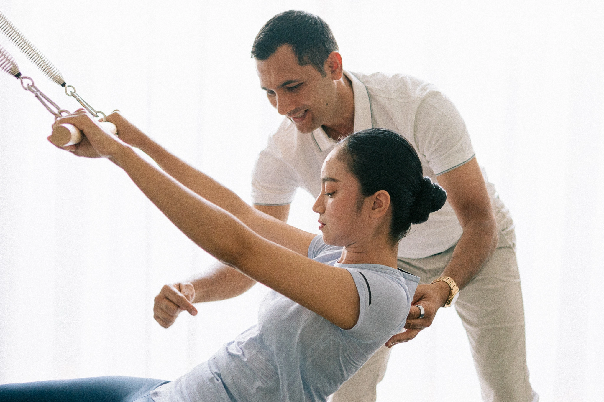 Clinical Pilates instructor assisting a woman during a reformer Pilates exercise session in a professional wellness studio